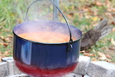 Ein großer blau-roter Topf mit Chili con Carne auf dem Lagerfeuer